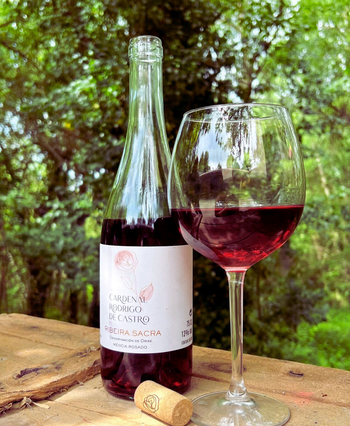 Glass of Cardenal Rodrigo de Castro Rosado poured beside the bottle outdoors in a garden setting